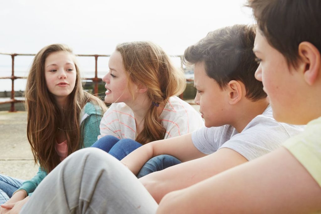 Grupo de adolescentes sentados al aire libre durante una dinámica de grupo que fomenta la comunicación y la cooperación.